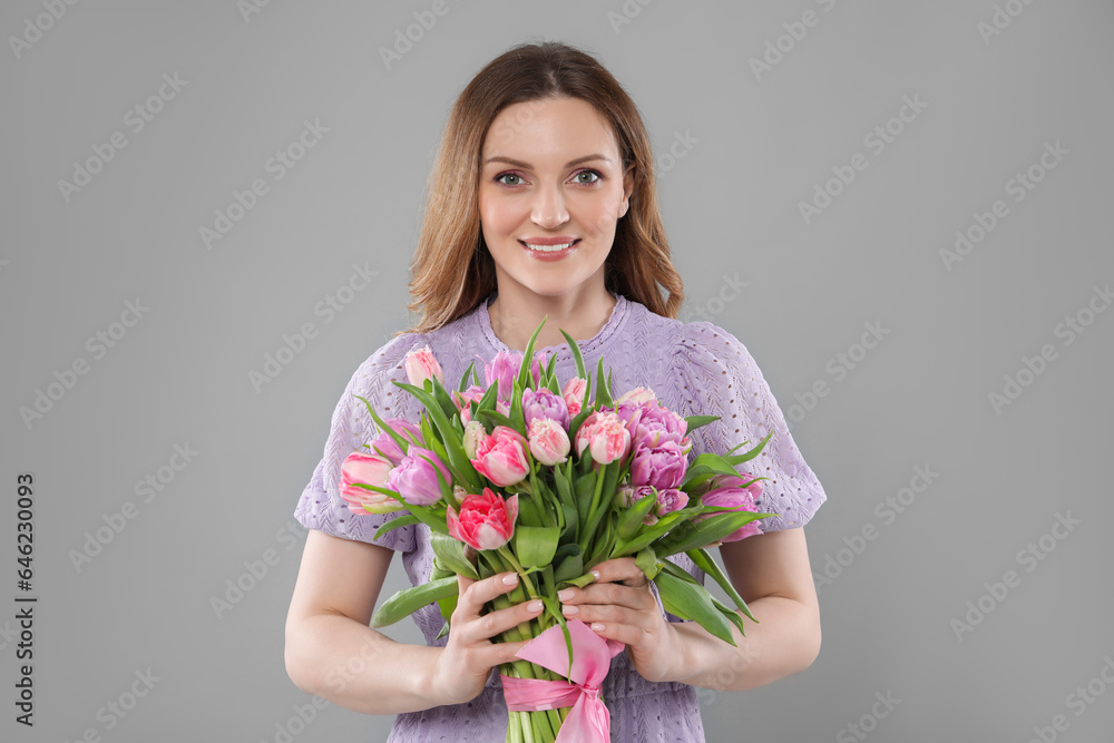 Happy young woman with bouquet of beautiful tulips on grey background