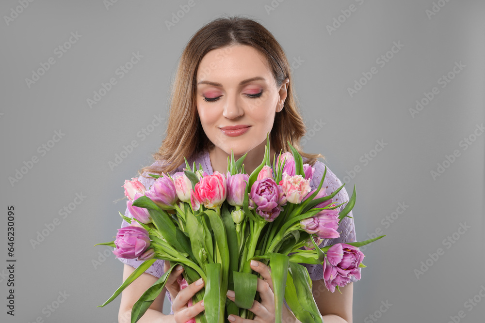 Happy young woman with bouquet of beautiful tulips on grey background