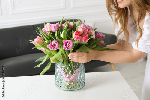 Woman putting bouquet of beautiful tulips in vase on white table indoors, closeup