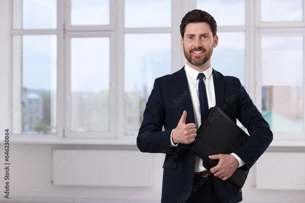 Happy real estate agent with leather portfolio showing thumb up in new apartment. Space for text Happy real estate agent with leather portfolio showing thumb up in new apartment. Space for text