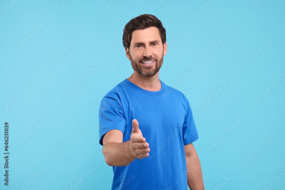 Happy man welcoming and offering handshake on light blue background Happy man welcoming and offering handshake on light blue background