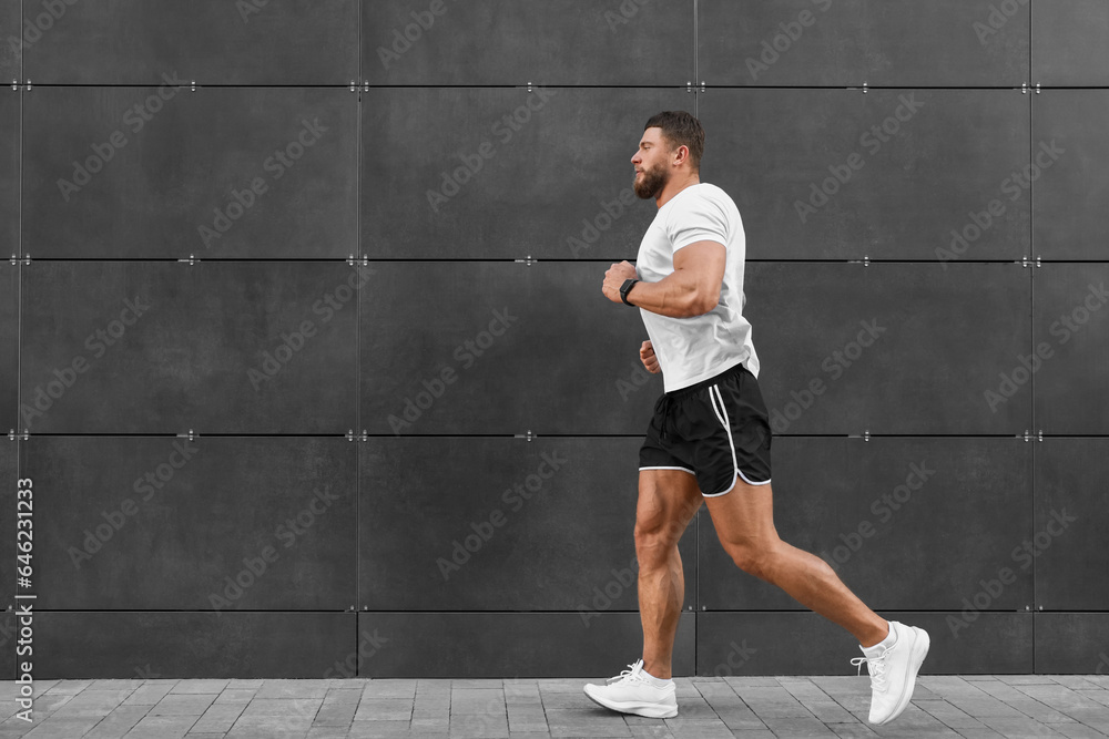 Fototapeta premium Young man running near building outdoors. Space for text