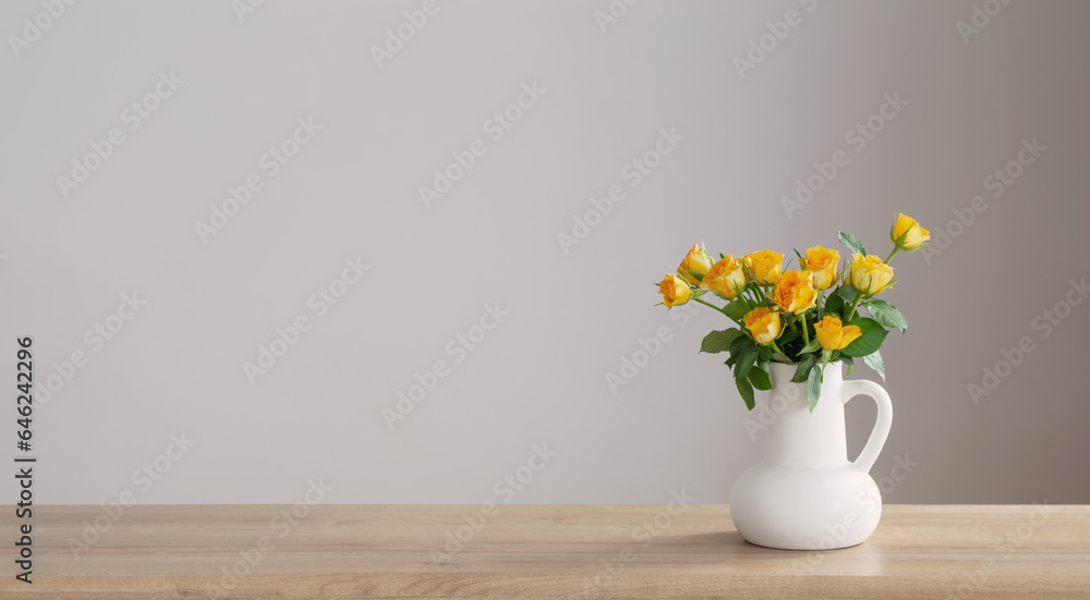 yellow roses in white jug on wooden shelf