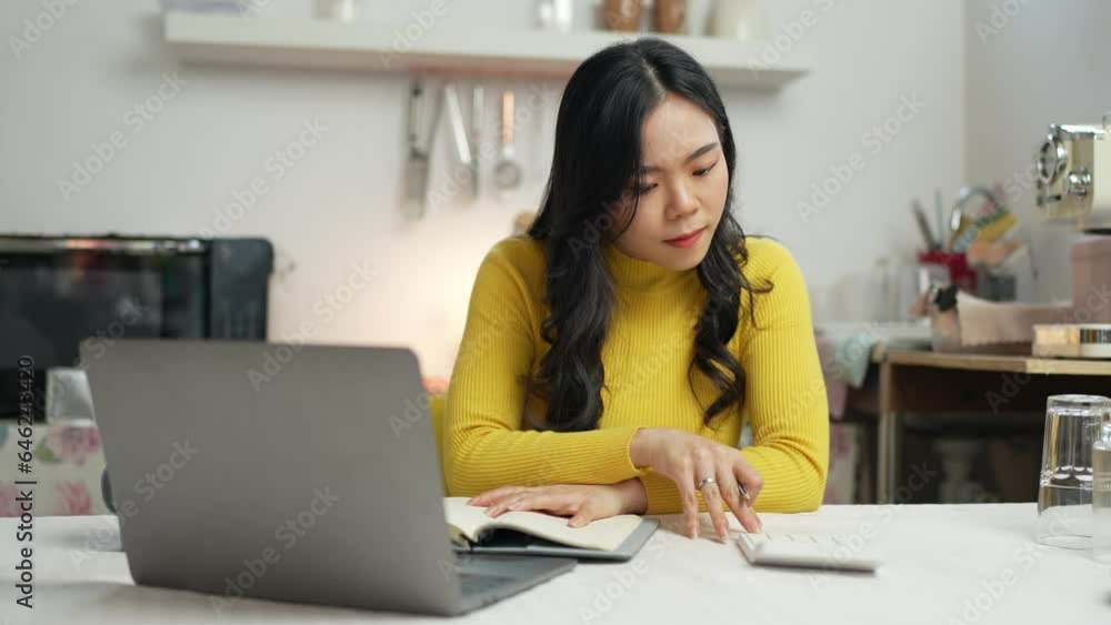 Smiling happy beautiful Asian woman relaxing using technology of laptop computer. take note of information Have a relaxing hot drink while sitting on the table in your room at home. Smiling happy beautiful Asian woman relaxing using technology of laptop computer. take note of information Have a relaxing hot drink while sitting on the table in your room at home.