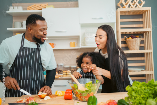 Kind African american parents teaching their adorable daughter how to cook healthy food  free space of kitchen  Happy black people family preparing healthy food in kitchen together