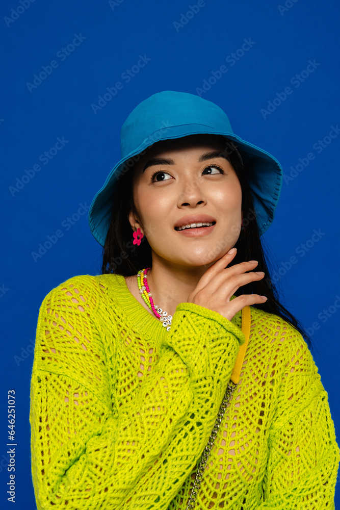 Beautiful asian woman posing while standing isolated over blue wall