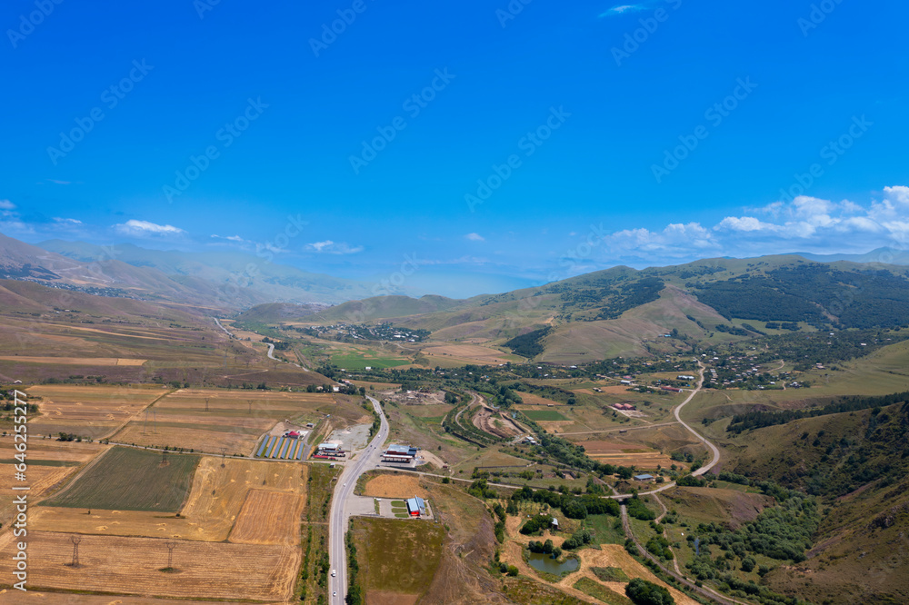 Beautiful aerial view on a road through a valley with clear blue skies and clouds over the mountains