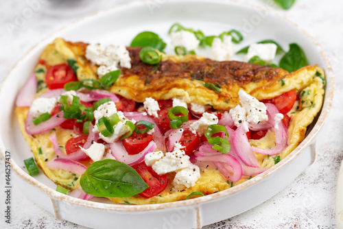 Omelette with tomatoes, feta cheese and red onion on white plate. Frittata - italian omelet.