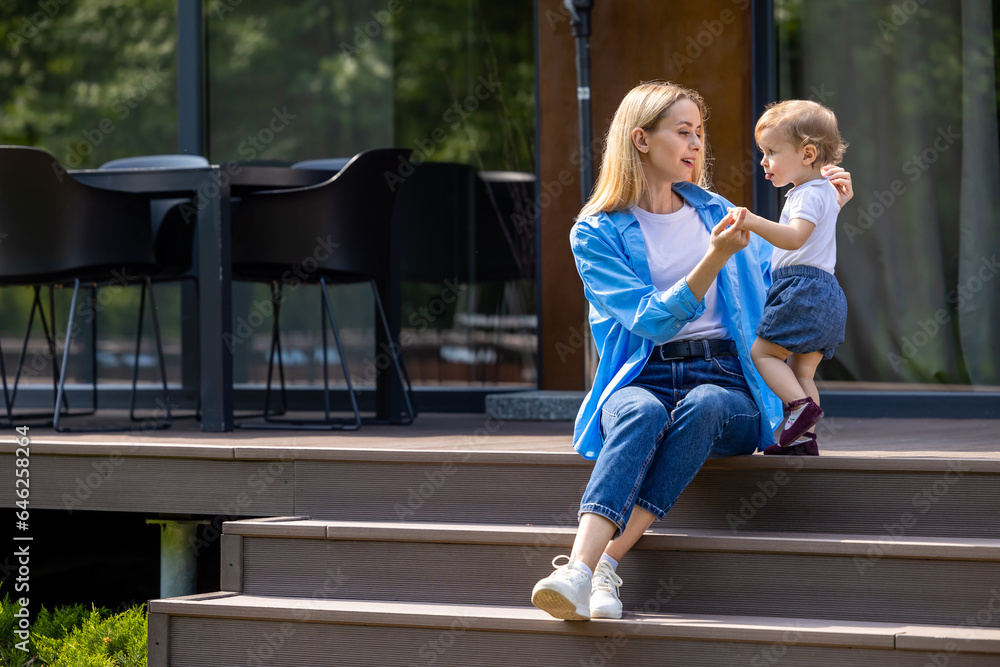 Blonde young woman sitting on the steps and playing with her kid Blonde young woman sitting on the steps and playing with her kid