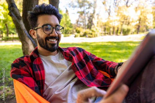Dark-haired young bearded man in checkered shirt lying in hammock