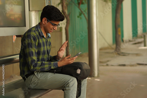 Young Indian middle class man sitting on bus stand using mobile phone