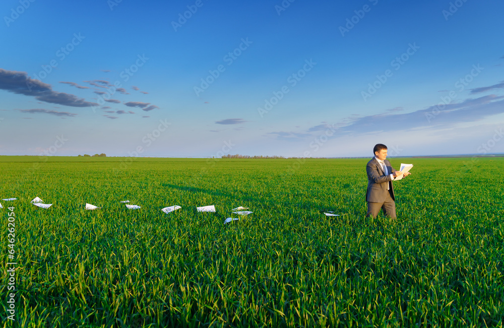 Fototapeta premium businessman lays out reports on a green grass field, the concept of work and freelancing
