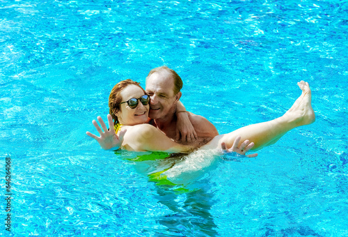 Bonding lovely mature caucasian couple having fun floating in outdoor swimming pool under the sun. Vacation, healthy lifestyle and relax concept