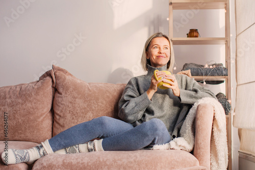 Happy dreamy middle aged woman sitting on sofa in living room with cup of tea or coffee photo