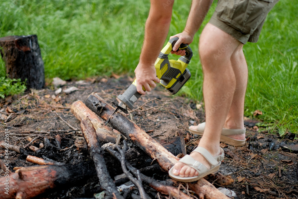 A man with an electrical saw cutting the firewood in the forest. A Sawmill employee cuts part of the tree pole and cleans the fireplace after use. A man with an electrical saw cutting the firewood in the forest. A Sawmill employee cuts part of the tree pole and cleans the fireplace after use.