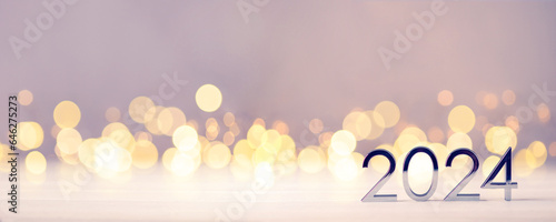 Metal numbers 2024 on a white table with Christmas trees and bokeh lights. Happy New Year 2024 is coming concept.