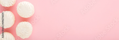Soft white vanilla zephyr on light pink table background. Pastel color. Closeup. Sweet snack. Food wide banner. Empty place for text. Top down view.