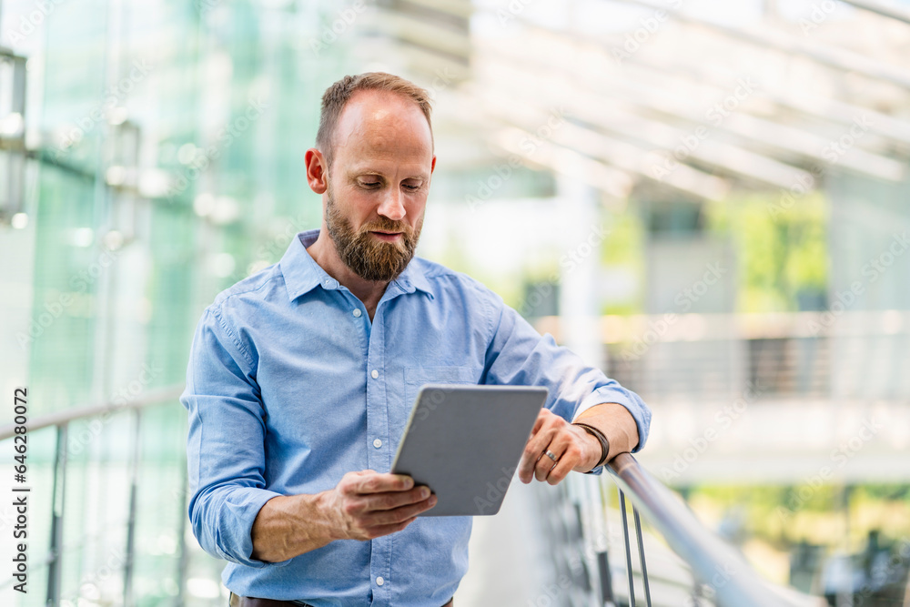 Experienced businessman using digital tablet standing in office building Experienced businessman using digital tablet standing in office building