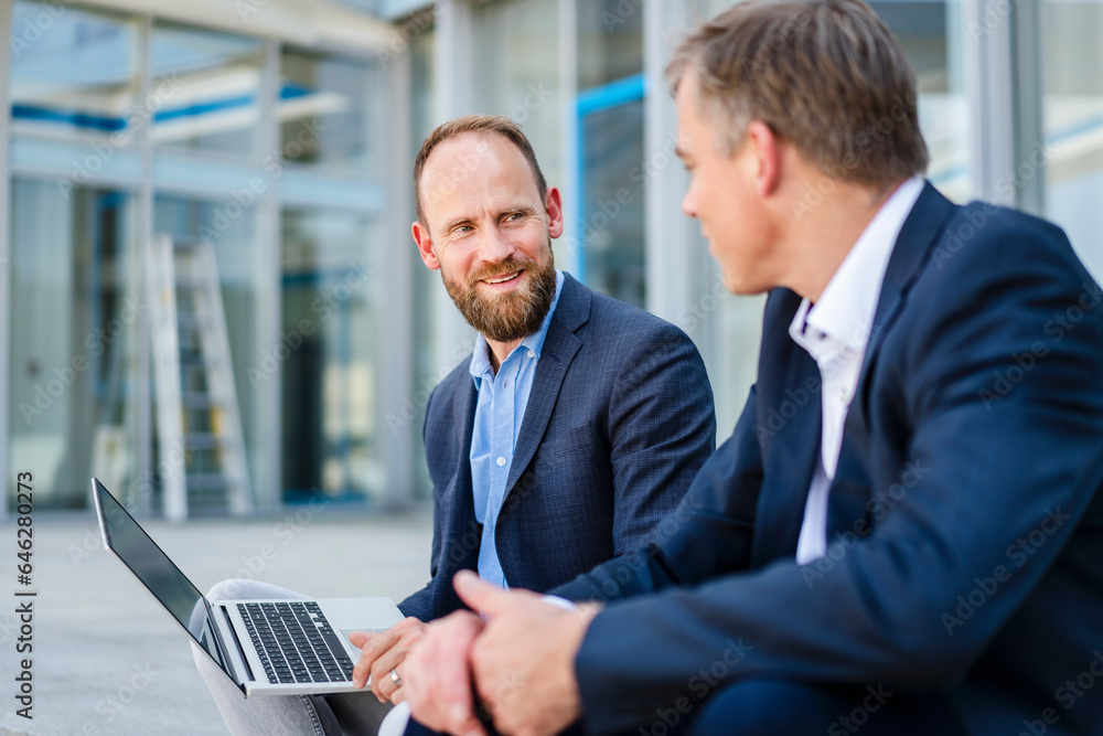 Two business colleagues sitting on steps working together on laptop Two business colleagues sitting on steps working together on laptop