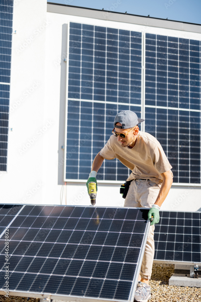 Man installing solar panels on the roof of his house, screwing cell on flat rooftop for self consumption. Renewable energy and sustainability concept Man installing solar panels on the roof of his house, screwing cell on flat rooftop for self consumption. Renewable energy and sustainability concept