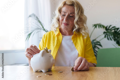 Smiling senior woman saving money in piggy bank at table photo