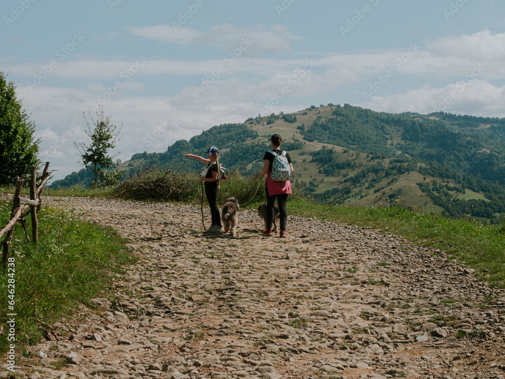 Obraz premium Family walk in Zakarpattya village Carpathian mountains view Ukraine Europe Scenic landscape green trees pets sunny day. Eco Local countryside tourism. Mother and daughter with dogs hiking Cottagecore