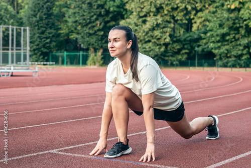 A young woman runner in start position on running track while work out.