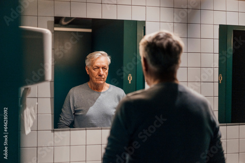 Senior man looking in mirror in bathroom photo