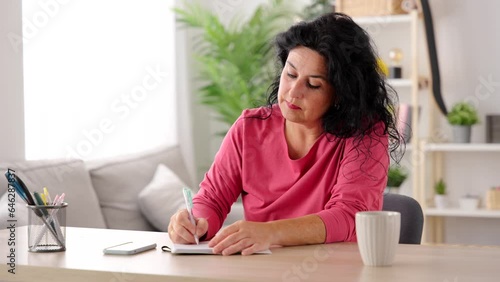 Middle aged woman writing diary on notebook.