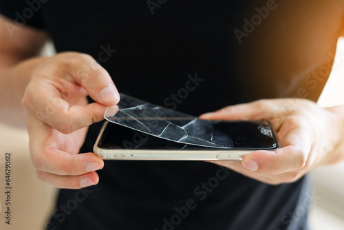 Process unrecognisable repairman is removing broken and old tempered glass screen protector from smartphone, close up view. Services for gluing and replacement of damaged protective glass.