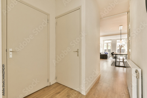 a hallway with white walls and wood flooring on the right side  there is an open door leading to another room