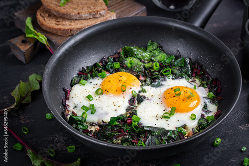 Breakfast. Fried eggs with green beet leaves, garlic, pepper and green onion in pan.
