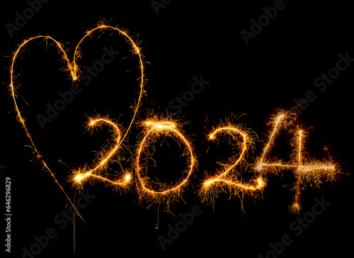Herz und Jahreszahl 2024 mit Wunderkerze geschrieben vor dunklem Hintergrund.