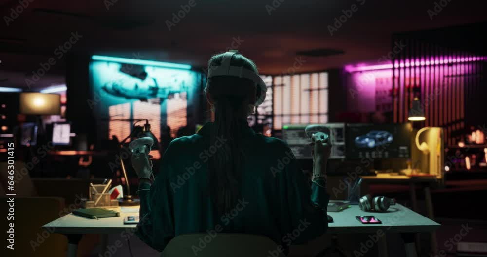 Back View of Young Woman Using Virtual Reality Headset with Controllers in her Creative Office at Night. Stylish Female Browsing Online, Spending Time in VR Software and Digital Platform Back View of Young Woman Using Virtual Reality Headset with Controllers in her Creative Office at Night. Stylish Female Browsing Online, Spending Time in VR Software and Digital Platform