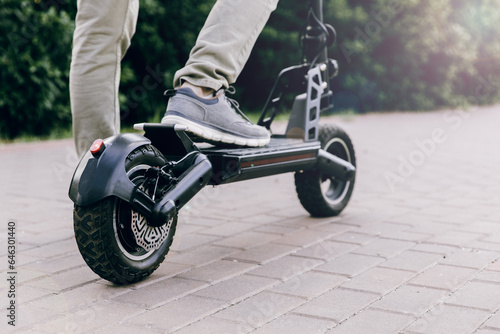 A man's foot stands on the platform of a scooter. Close-up of a man riding a black electric scooter. Walking and outdoor sports. Economical and environmentally friendly appliances for transportation.
