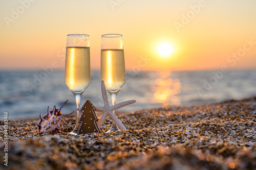 Fototapeta Naklejka Na Ścianę i Meble -  Two glasses and a Christmas tree with a shell and a starfish on the seashore. Christmas romantic evening on the beach. Selective focus. Christmas card