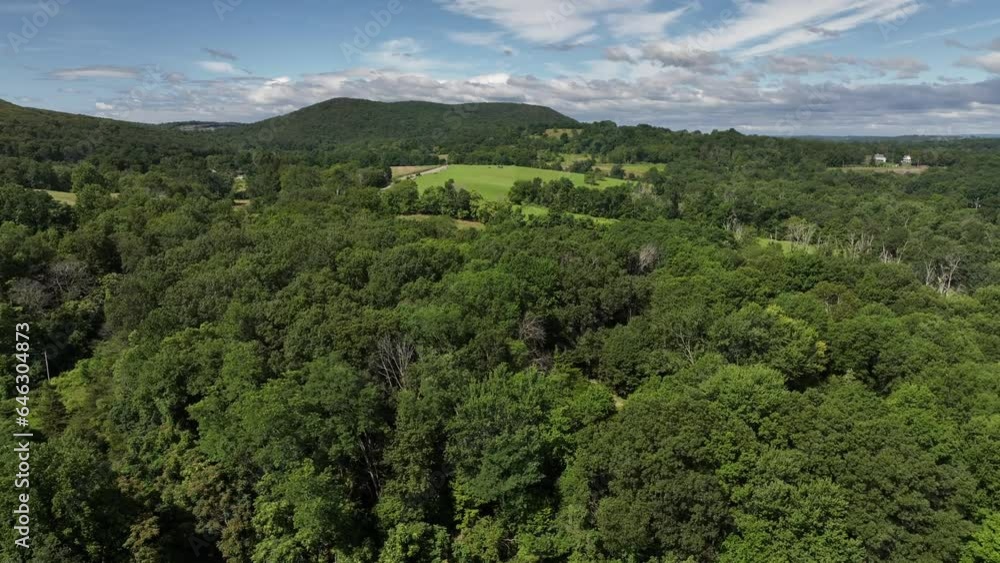 A high angle, aerial view of the hills and valleys of Salisbury Mills, NY on a beautiful and sunny day with blue skies and white clouds. The drone camera dolly in, just over the tree tops and fields. A high angle, aerial view of the hills and valleys of Salisbury Mills, NY on a beautiful and sunny day with blue skies and white clouds. The drone camera dolly in, just over the tree tops and fields.