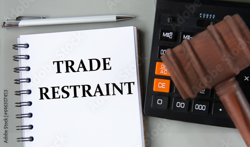 TRADE RESTRAINT - words in a white notebook on the background of a calculator and a judge's gavel