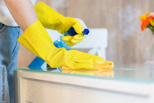 Woman in rubber gloves sprays cleanser and wipes table with rag. Close up. Cleaning service and chores