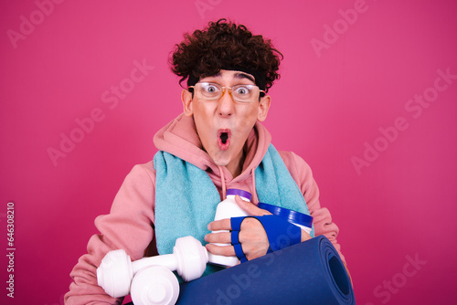 Young attractive curly man posing on a pink background and doing fitness.