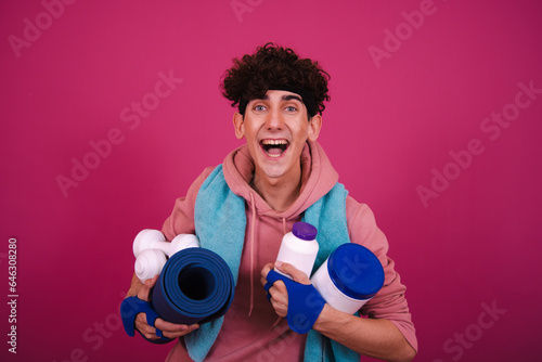 Young attractive curly man posing on a pink background and doing fitness.