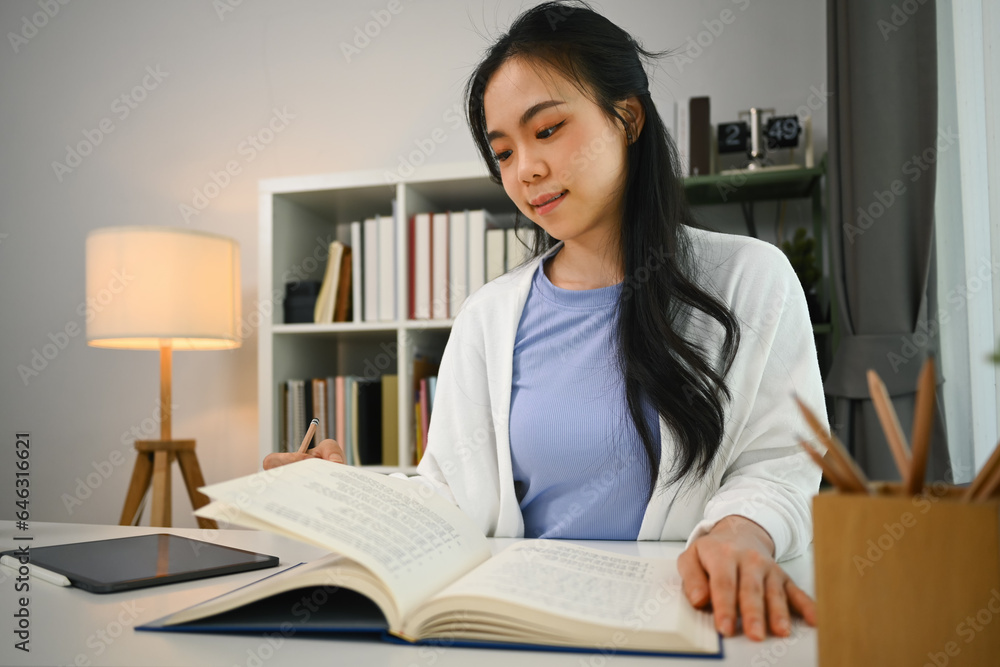 Charming asian fe male student reading book, preparing for exam or, doing homework in living room Charming asian fe male student reading book, preparing for exam or, doing homework in living room