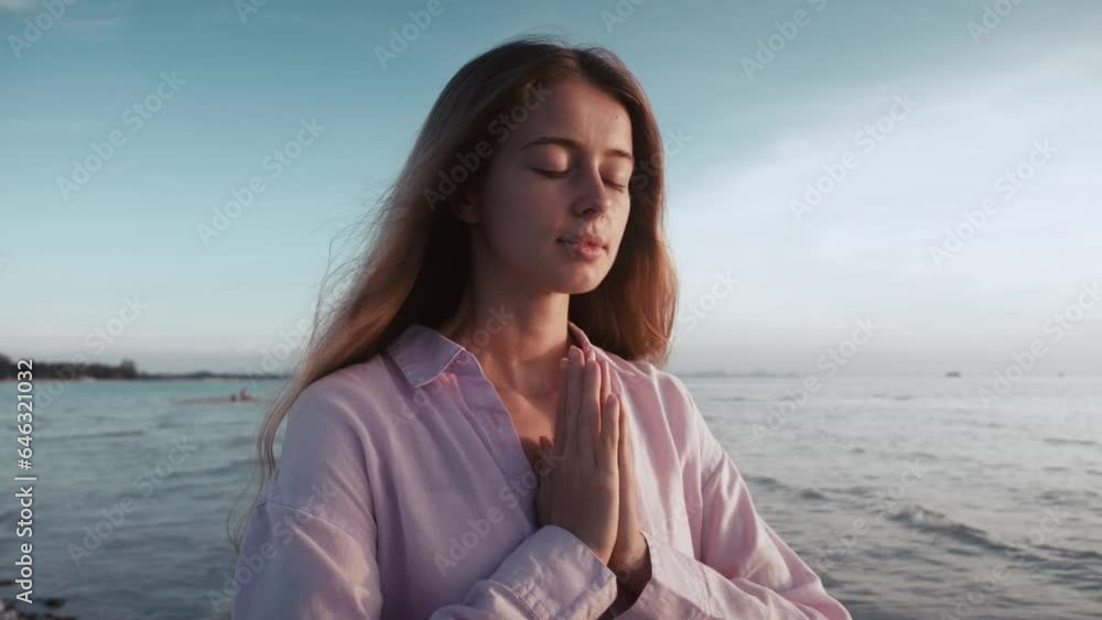 Serene woman praying with closed eyes in nature at sea sunrise background. Religion, spiritual and peace concept. Girl folded hands in prayer silhouette in the morning on sea sunrise. Morning prayer. Serene woman praying with closed eyes in nature at sea sunrise background. Religion, spiritual and peace concept. Girl folded hands in prayer silhouette in the morning on sea sunrise. Morning prayer.