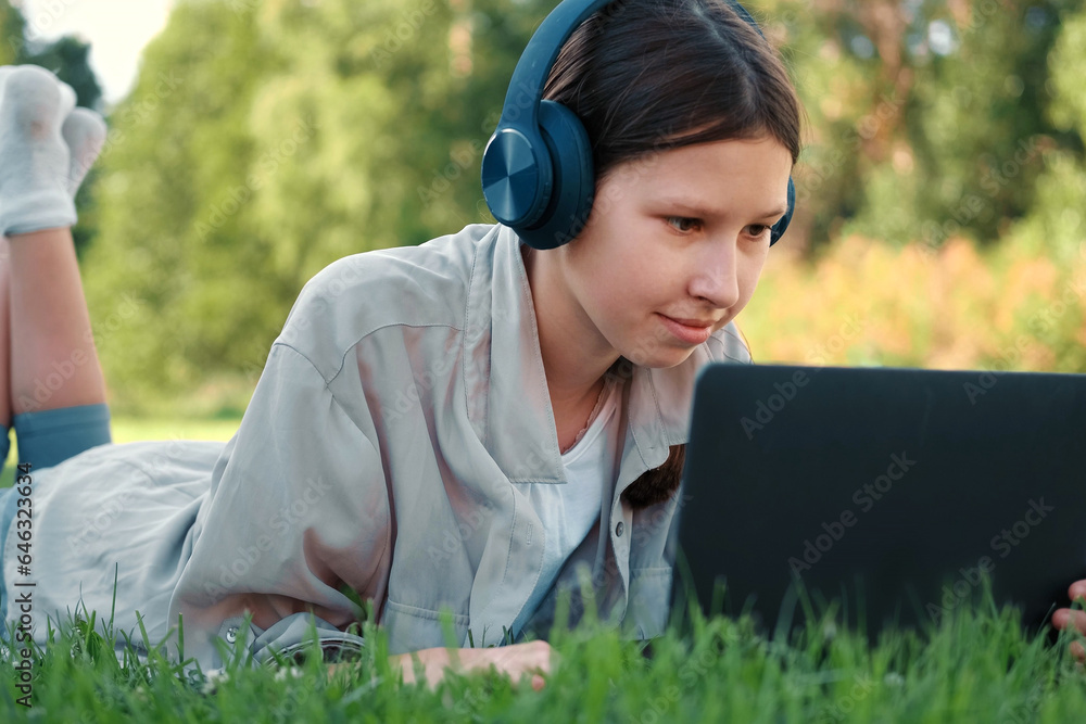 Teenage schoolgirl studying reading her books, tablet and notebook, sitting outdoors. Back to school. Student girl lying on the green grass using laptop in the college yard or park. Distance learning. Teenage schoolgirl studying reading her books, tablet and notebook, sitting outdoors. Back to school. Student girl lying on the green grass using laptop in the college yard or park. Distance learning.