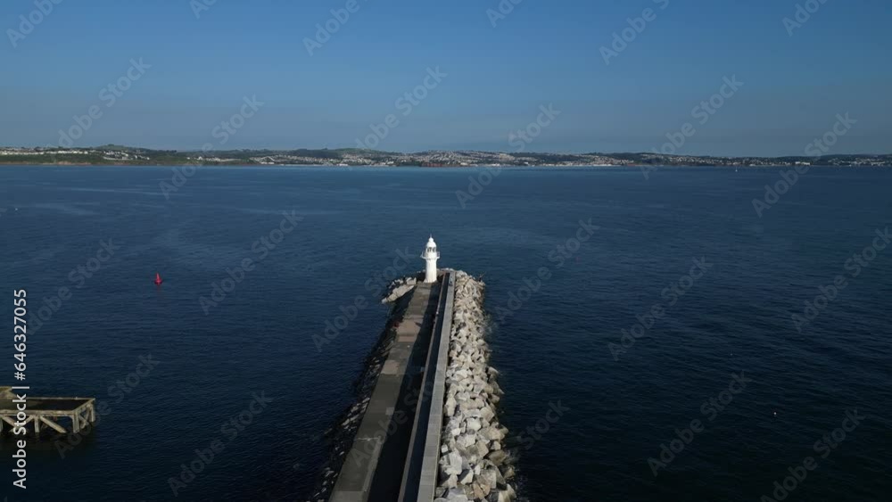 Brixham, Torbay, South Devon, England: DRONE VIEW: Drone reverse flies over Brixham Harbour Lighthouse then parallel to the Wall. Brixham is a popular UK summer holiday resort and tourist destination. Brixham, Torbay, South Devon, England: DRONE VIEW: Drone reverse flies over Brixham Harbour Lighthouse then parallel to the Wall. Brixham is a popular UK summer holiday resort and tourist destination.