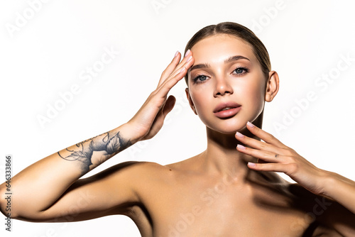 Beauty of an attractive smiling sensual young woman standing isolated over gray background, touching her face, posing