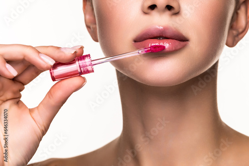 Fényképezés Young woman applying lipstick with an applicator on white background