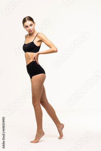 Full-length portrait of young slim woman posing in black underwear isolated over grey background.