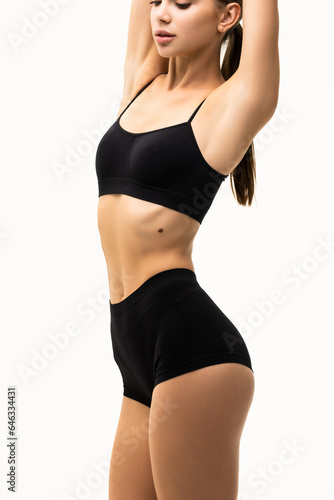 Beautiful sporty woman in black bikini posing on grey background. Beauty and body care concept
