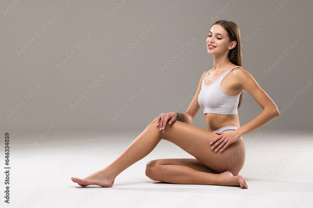 Fototapeta premium Young beautiful woman with perfect body in underwear sitting on floor posing on white studio background.